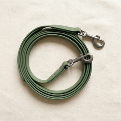 A moss-green coated waterproof dog lead with matte trigger clip, coiled on cream linen