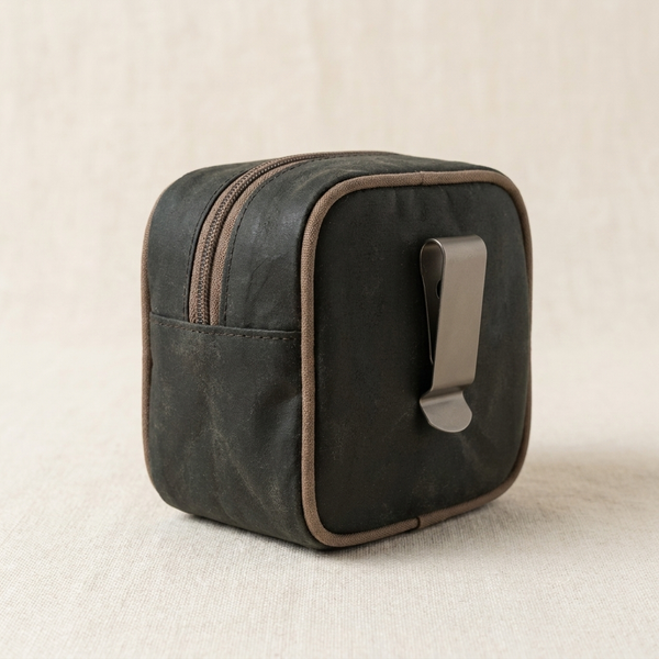 A peat-dark waxed canvas dog treat pouch with belt clip, on cream linen