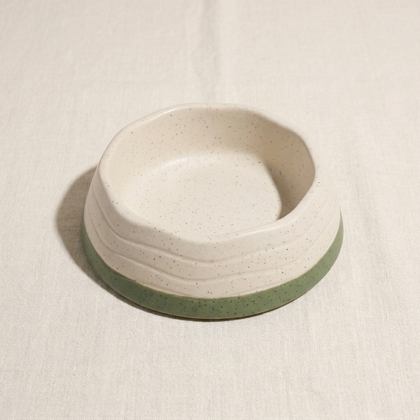 A cream and moss speckled plant-based dog bowl, on cream linen